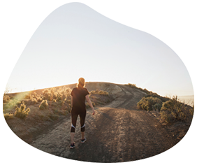 A person in athletic clothing walks on a dirt path surrounded by lush vegetation at sunset, near the serene landscapes of Saddleback in Peoria, AZ.