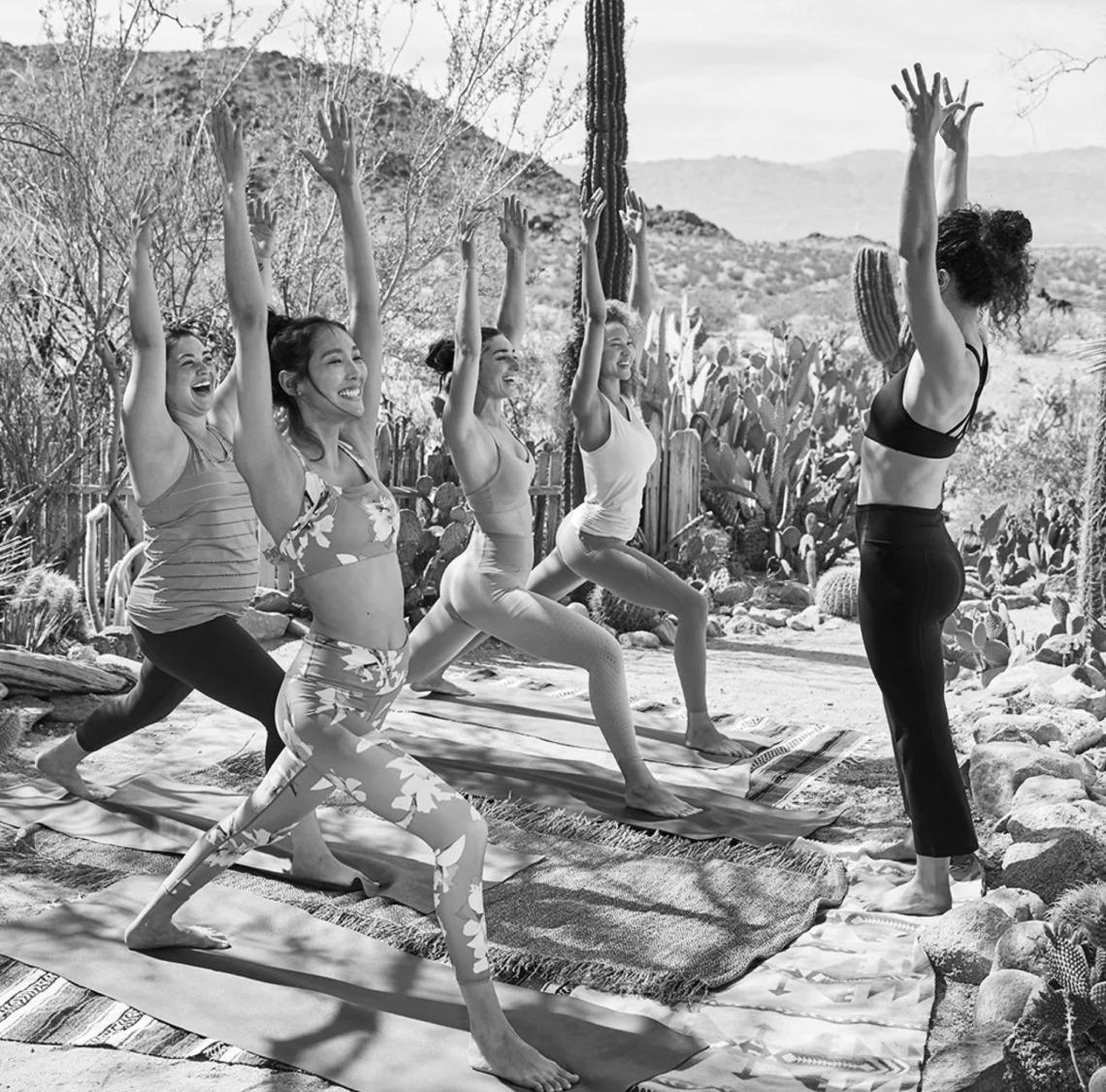 A group of people practice yoga in warrior pose outdoors, surrounded by desert plants and cacti, with the stunning backdrop of Peoria AZ.