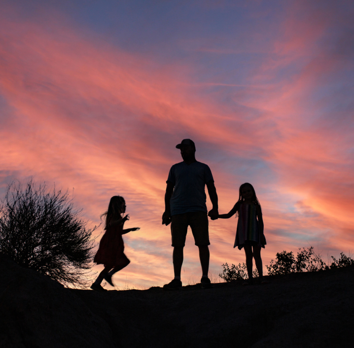 Silhouette of an adult and two children holding hands against a colorful sunset sky in Peoria, AZ, where new homes offer families the perfect place to create lasting memories.